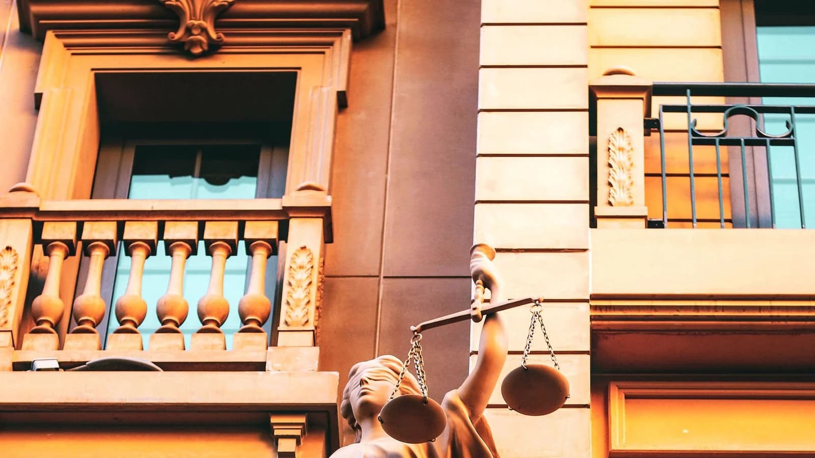 Statue of Lady Justice holding scales on a building facade, symbolizing law and fairness.