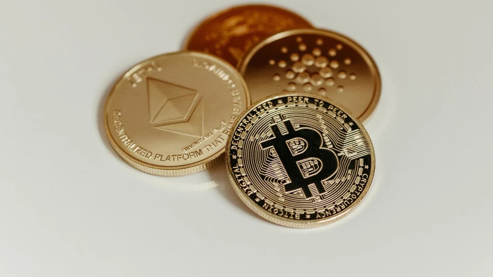 Cryptocurrency coins representing Bitcoin, Ethereum, and Cardano on a white background.