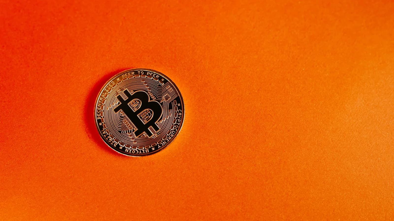 Close-up of a Bitcoin coin on a vivid orange background, symbolizing digital currency.
